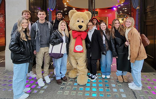 Group of students posing outside Hamleys with a big teddy bear