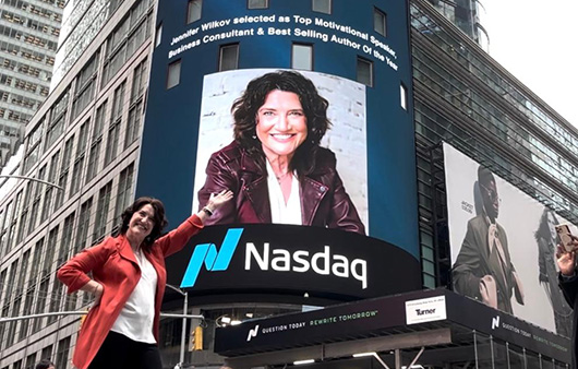 Jennifer Wilkov posing in front of Nasdaq billboard